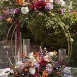 Two floral centerpieces on gold hoops with candles on a table