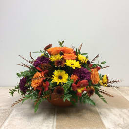 Low floral arrangement with orange roses, yellow daisies, and purple blooms in a bowl vase