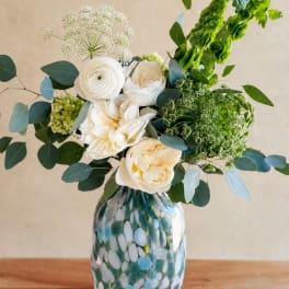White flowers in a patterned glass vase with blue-green foliage