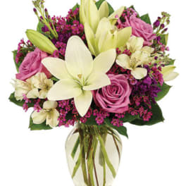 Bouquet of pink roses, white lilies, and purple filler in a glass vase
