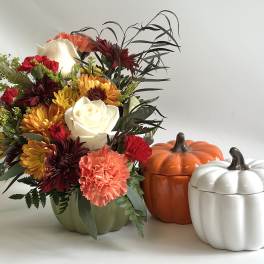 Mixed autumn bouquet in a green vase beside two pumpkin containers