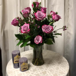 Pink roses arranged in a glass vase with two purple candles beside it