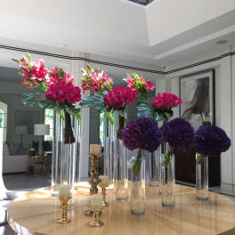 Tall floral centerpieces with pink lilies, roses, and purple hydrangeas in glass vases
