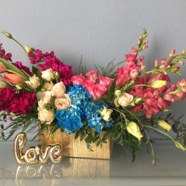 Colorful flower arrangement in a gold box with a small gold "love" decoration