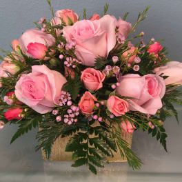 Pink roses and spray roses arranged in a gold rectangular container