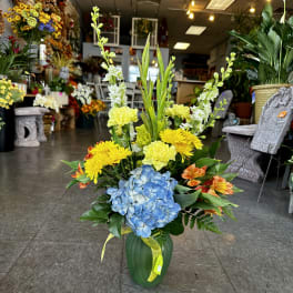 Tall mixed flower arrangement in a green vase with blue hydrangea and yellow blooms
