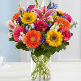 Mixed bouquet of roses, lilies, sunflowers, and gerbera daisies in a glass vase
