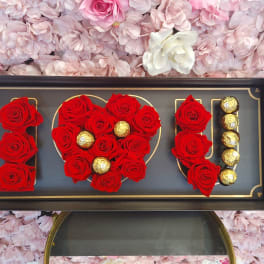 Red roses and gold chocolates arranged in a framed display spelling love.