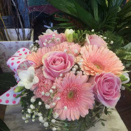 Pink roses and gerbera daisies in a glass vase with a polka-dot ribbon