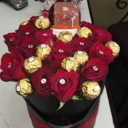 Red roses and gold-wrapped chocolates arranged around a wine bottle in a black box