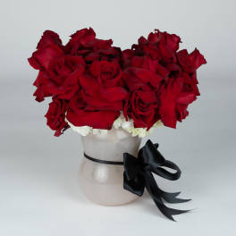 Red rose arrangement in a white vase with a black ribbon