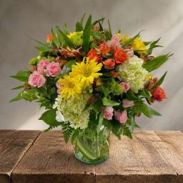 Mixed bouquet of pink and orange roses with yellow daisies in a glass vase