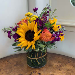 Bright mixed bouquet with sunflowers, roses, and purple blooms in a glass vase
