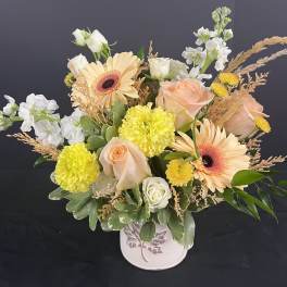 Mixed bouquet of peach roses, gerbera daisies, and yellow carnations in a white vase