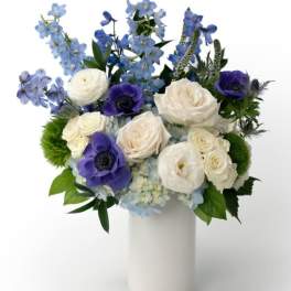 White and blue flower arrangement with roses and anemones in a tall white cylinder vase