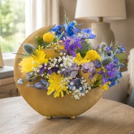 Mixed bouquet in a gold crescent vase with yellow, blue, and purple flowers