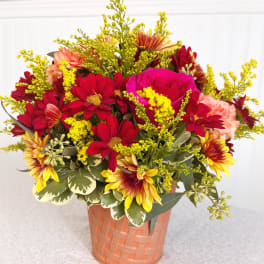 Mixed bouquet of red, pink, and yellow flowers in a peach basket vase