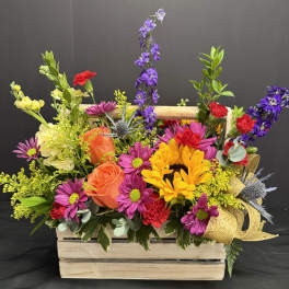 Mixed bouquet in a wooden crate with sunflowers, roses, and purple blooms