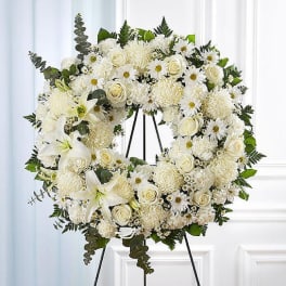 White floral wreath on a black stand with roses, daisies, and lilies