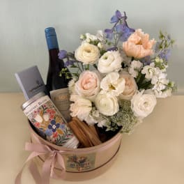 Flower arrangement in a round gift box with wine and tea tins