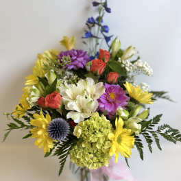 Mixed bouquet of yellow daisies, roses, and purple flowers in a glass vase