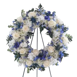 Circular floral wreath with white roses and blue flowers on a stand