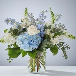 Blue hydrangea and white flower arrangement in a clear glass vase