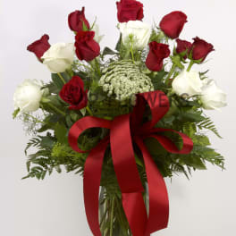 Red and white roses in a glass vase with a red ribbon