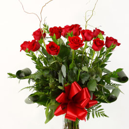 Red roses arranged in a clear glass vase with a red bow