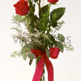 Three red roses in a tall glass vase with a red ribbon