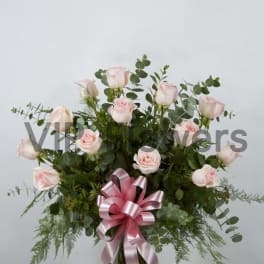 Pink roses arranged in a glass vase with a pink ribbon bow