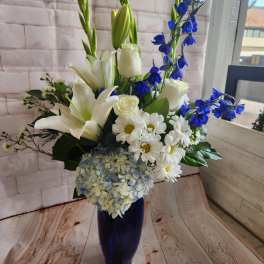 White lilies, roses, daisies, and blue flowers in a dark blue vase
