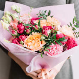 Bouquet of pink, peach, and white roses with carnations wrapped in pale pink paper