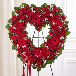 Heart-shaped red rose wreath on a stand with a ribbon bow