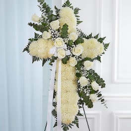 White floral cross arrangement with roses and ribbon on a stand