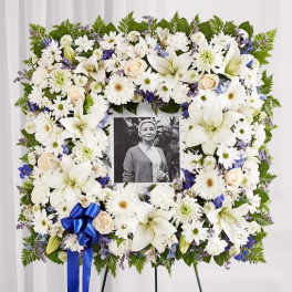 White floral funeral wreath with a photo in the center and blue ribbon