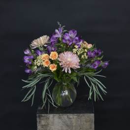 Mixed bouquet of purple, peach, and pink flowers in a glass vase