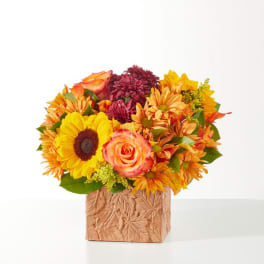 Mixed bouquet with sunflowers, roses, and mums in a textured square vase