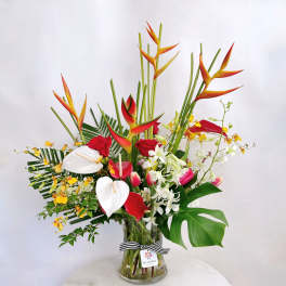 Tall tropical bouquet with red roses, white anthuriums, and orange heliconia in a glass vase