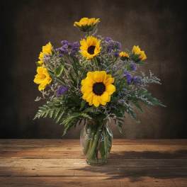 Sunflowers arranged in a clear glass vase with purple filler flowers