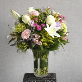 Mixed bouquet of white lilies, roses, and pink flowers in a glass vase