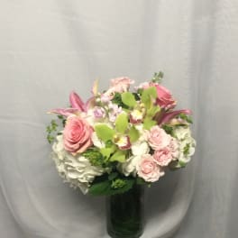Round arrangement of pink roses, green orchids, and white hydrangeas in a clear glass vase