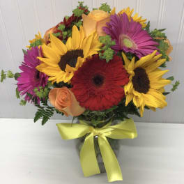 Bouquet of sunflowers, gerbera daisies, and roses in a glass vase with a yellow ribbon
