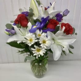 Mixed bouquet of red roses, white lilies, and daisies in a glass vase