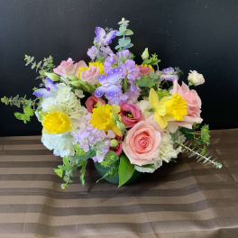 Mixed bouquet of pink, yellow, white, and purple flowers in a low container