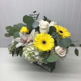 Bouquet of white roses, yellow gerbera daisies, and orchids in a glass vase