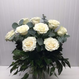 Tall arrangement of ivory roses with abundant greenery in a clear glass vase
