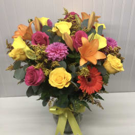 Bright mixed bouquet of roses, lilies, and gerbera daisies in a glass vase