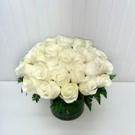 Low round arrangement of creamy white roses clustered in a clear glass cylinder vase