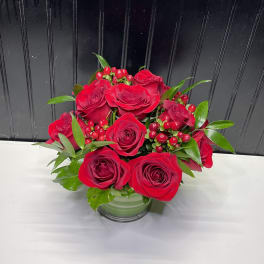 Red roses arranged in a clear glass vase with red berries